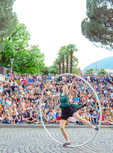 Akrobatin performt mit großem Cyr-Rad vor begeistertem Publikum auf einem Platz im Freien bei einem Event der Therme Meran